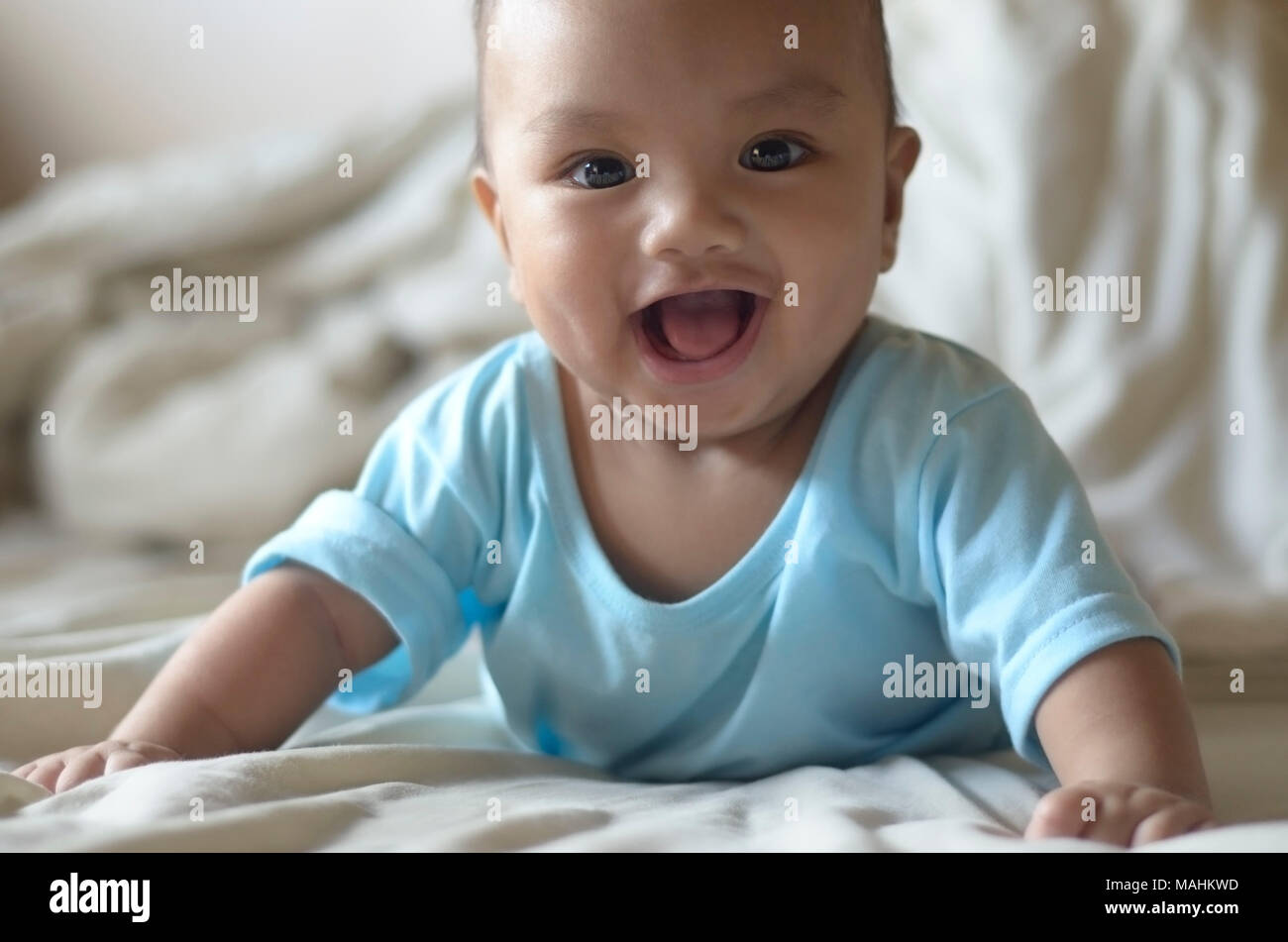 The photographer`s own son photographed when he was five months old. The infant is smiling in a semi-prone position or half-lying on his stomach . Stock Photo